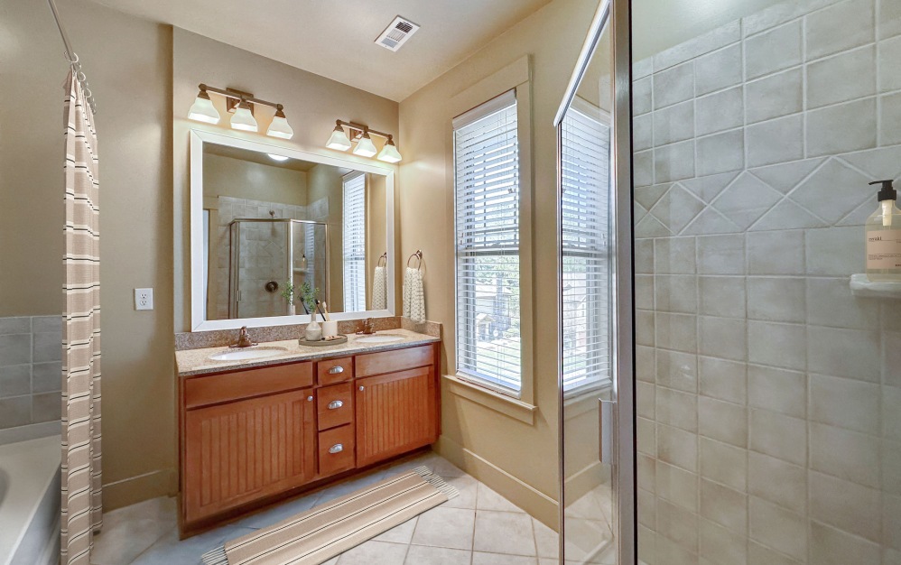 Apartment bathroom with double vanity sinks, a large mirror, and glass encased shower